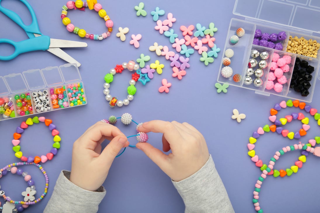 Little girl made bracelets on purple background. Kids handmade beaded jewelry. DIY bracelet beads.